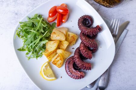 Grilled octopus with fried potatoes, arugula, tomatoes and lemon. Close-up.の写真素材