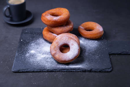 Donuts with powdered sugar and a cup of coffee. Traditional donuts in the shape of a ring fried in oil, on a black background. Junk food. Close-up.の写真素材