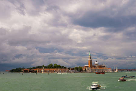 Basilica of San Giorgio Maggiore at sunset. Boats are sailing along the canal. Summer evening, dark clouds in the sky. Italy, Venice.の写真素材