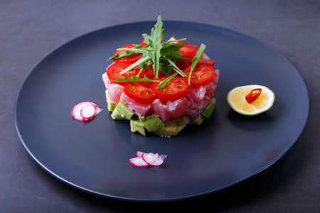 Fresh tuna tartare with avocado, arugula, cherry tomatoes, radish, chili and lime. Traditional cold appetizer of French cuisine. Close-up, selective focus.の写真素材