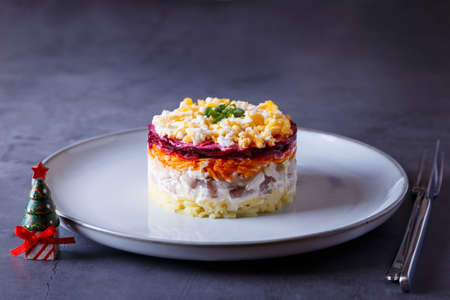 Herring salad under a fur coat. Traditional Russian multilayered salad from herring, beets, potatoes, carrots and eggs. Close-up, gray background, miniature Christmas tree.の写真素材