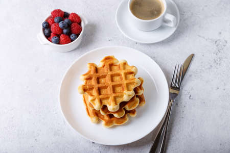 Viennese or Belgian waffles with fresh berries (raspberries and blueberries) on a white plate and a cup of coffee. Traditional dessert. Close-up, white background, top view.の写真素材