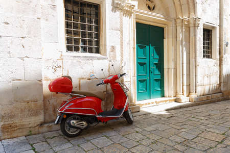 Red moped (scooter) is parked near the entrance to the building. Croatia, city of Trogir, sunny...
