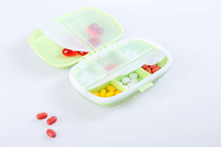 Pill box with colorful pills and vitamins. Plastic green container with cells for medicines. health concept. Selective focus, close-up.の写真素材