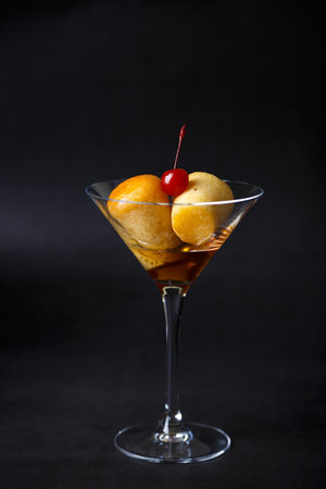 Neapolitan Rum baba (or baba au rum) in a martini glass with a cocktail cherry on a black background. Small yeast cakes soaked in rum syrup. Traditional Italian pastry. Close-up, selective focus.の写真素材
