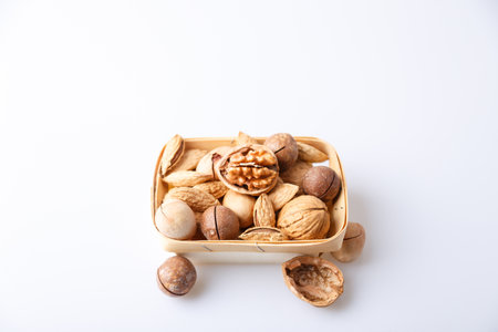 Assorted nuts in the shell on a white background: walnuts, pecans, almonds, macadamia. Nuts in a basket. Selective focus, close-up. Place for text.の写真素材