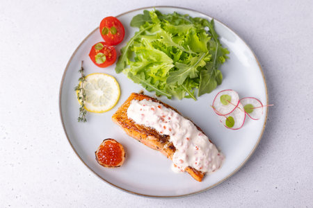 Salmon (trout) with creamy Champagne sauce with red caviar, arugula, cherry tomatoes, radish and lemon. Traditional French dish. Selective focus, close-up, top view.の写真素材