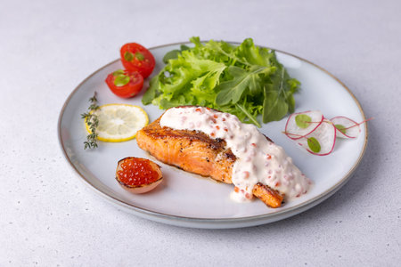 Salmon (trout) with creamy Champagne sauce with red caviar, arugula, cherry tomatoes, radish and lemon. Traditional French dish. Selective focus, close-up.の写真素材