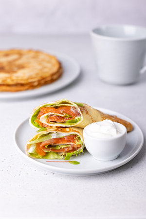 Pancakes with salmon (trout), sour cream and greenstuff. Thin, not sweet blinchiki stuffed with red fish. Traditional Russian and Ukrainian dish. Feast of Maslenitsa. Selective focus, close-up.の写真素材