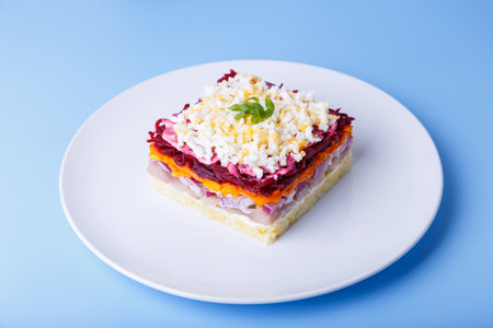 Herring salad under a fur coat. Traditional Russian multilayered salad from herring, beets, potatoes, carrots and eggs. Close-up, blue background.の写真素材