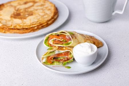 Pancakes with salmon (trout), sour cream and greenstuff. Thin, not sweet blinchiki stuffed with red fish. Traditional Russian and Ukrainian dish. Feast of Maslenitsa. Selective focus, close-up.の写真素材