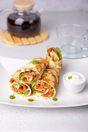 Pancakes with salmon (trout), sour cream, greenstuff and tea. Thin, not sweet blinchiki stuffed with red fish. Traditional Russian and Ukrainian dish. Feast of Maslenitsa. Selective focus, close-up.の写真素材