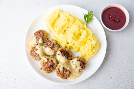 Swedish noisettes (fricandel) with mashed potatoes, Brune Sos creamy sauce and lingonberry (cranberry) sauce. Traditional meatballs with garnish. Selective focus, top view, close-up.の写真素材
