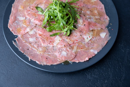 Marbled beef carpaccio with arugula, parmesan cheese, olive oil and lemon. A traditional classic appetizer made from thinly sliced raw meat. Close-up, selective focus, top view, black background.の写真素材