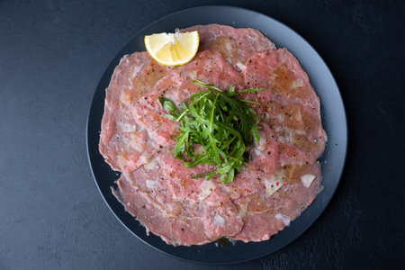 Marbled beef carpaccio with arugula, parmesan cheese, olive oil and lemon. A traditional classic appetizer made from thinly sliced raw meat. Close-up, selective focus, top view, black background.の写真素材