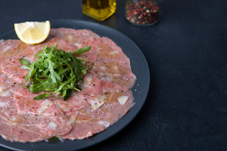 Marbled beef carpaccio with arugula, parmesan cheese, olive oil and lemon. A traditional classic appetizer made from thinly sliced raw meat. Close-up, selective focus, black background.の写真素材