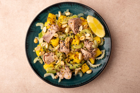 Salad with canned tuna, peanuts, mango, avocado, celery, chili flakes and black sesame. Light summer salad with olive oil and a lemon lobule. Home cooking. Selective focus, close-up.の写真素材
