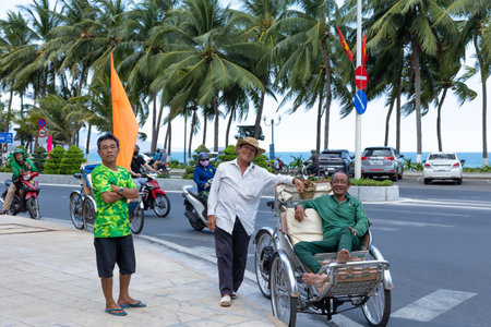 Nha Trang, Vietnam - April 22, 2024: Vietnamese elderly men pose on the street and smile. Rickshaw driver sits in his cart. Sea and palm trees are in the background. Selective focus.のeditorial素材