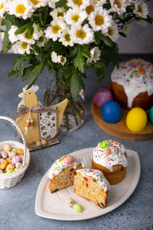Two small Easter kulichs with candied fruits in white glaze with colorful sprinkles in the cut. Painted chicken and quail eggs. Traditional Easter baking. Easter holiday. Close-up, selective focus.の写真素材