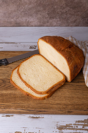 Wheat (white) bread with a crispy crust on a wooden board, cut into slices. Homemade baking in rustic style. Selective focus, close-up.の写真素材
