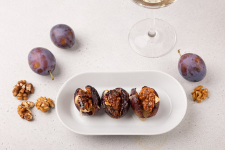 Plums baked with Camembert cheese, walnuts, honey and glass of white wine. Popular hot appetizer on a black plate. Selective focus, close-up.の写真素材