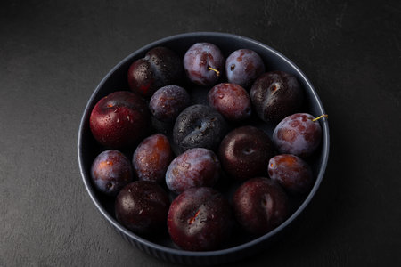 Juicy ripe fresh plum with water drops in gray plate on black background. Seasonal fruits. Selective focus, close-up.の写真素材
