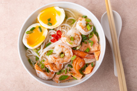 Asian dish with broth, noodles, tiger shrimp, fish, egg and green onions. Traditional Asian soup in a white deep plate. Selective focus, close-up.の写真素材