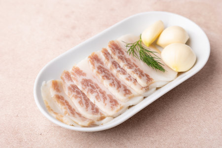 Homemade salted pork lard, sliced, with garlic cloves on a white plate. Traditional appetizer for vodka, borsch, shchi, soup. Homemade dish made from subcutaneous pig fat.の写真素材