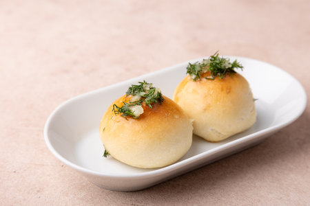 Sweet little buns with garlic and dill on a white plate. Pampushki for breakfast, with borsch or with soup. Traditional homemade baking. Selective focus, close-up.の写真素材