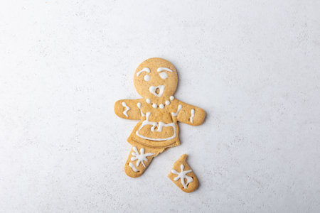 Gingerbread man with a broken leg (without leg) and with a surprised face. Traditional New Year and Christmas homemade cookies on a white background. Selective focus, close-up.の写真素材