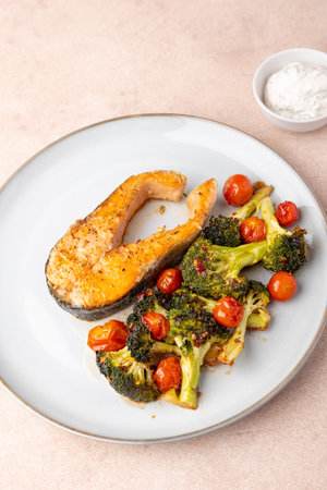 Fried salmon steak (trout) with baked broccoli and cherry tomatoes. Served with sour cream sauce with dill. Traditional home cooking. Selective focus, close-up.の写真素材