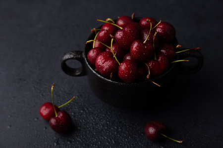 Juicy ripe fresh cherries with water drops in a black plate on a black background. Seasonal fruits, harvest. Selective focus, close-up.の写真素材