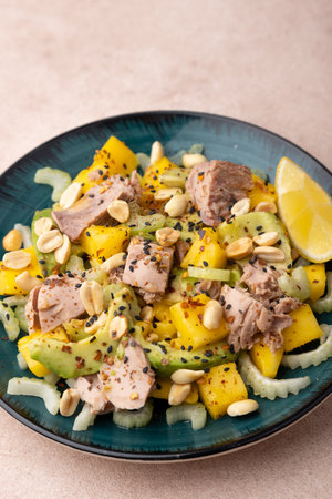 Salad with canned tuna, peanuts, mango, avocado, celery, chili flakes and black sesame. Light summer salad with olive oil and a lemon lobule. Home cooking. Selective focus, close-up.の写真素材