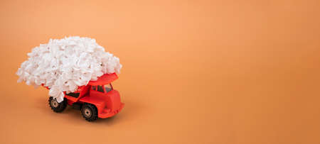 Toy truck in orange, loaded with white lilacs on a colored background. Bannerの写真素材