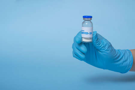 Medical concept: a doctor's hand in a blue medical glove holds a bottle of injectable medicine or...