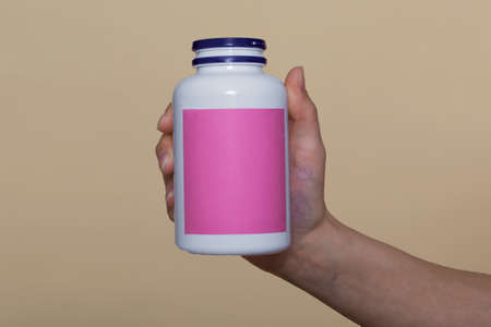 close-up, on a beige background. the girl holds vitamins in a white bottle in her hand. vitamins for immunity, recovery. vitamins for beauty. space for textの写真素材