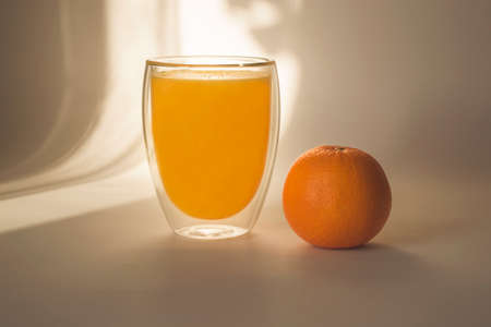 Glass of orange juice and orange on a light background in the shadeの写真素材