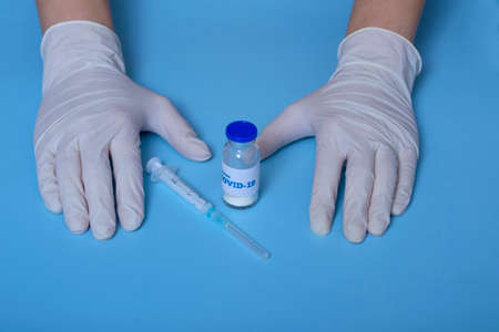 Medical concept. On a blue background doctor's hands in white gloves, coronavirus vaccine, syringe. virus protection.Concept: prevention of coronavirusの写真素材