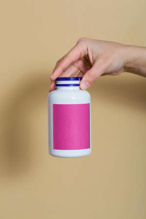 close-up, on a beige background. the girl holds vitamins in a white bottle in her hand. vitamins for immunity, recovery. vitamins for beauty. place for text. vertical photoの写真素材