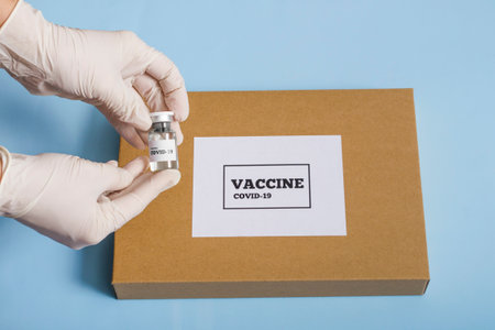 medical concept box with coronavirus vaccine. A doctor's hand in a white glove holds a bottle of covid 19 vaccine or medicine on a blue background.の写真素材
