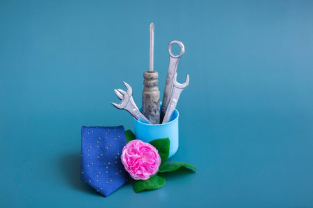 Creative vase with tools: screwdriver, wrench. On a colored background, a pink rose, a blue tie and a vase with tools. Minimalism for Father's Day. Close-up, monochrome. Still lifeの写真素材
