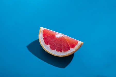 Creative concept. Sliced ââjuicy orange grapefruit with shadow isolated on blue background. Tropical fruit minimal composition.の写真素材