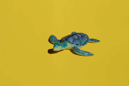 Summer bright concept - blue toy turtle on a yellow background.