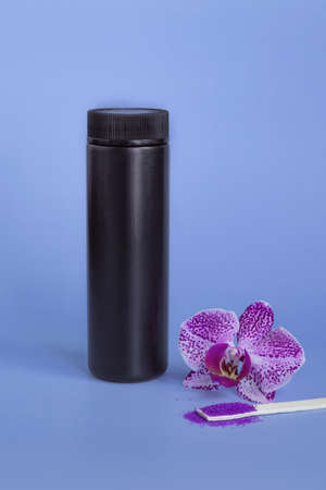 Spa mockup: purple cosmetic sea salt spa, black plastic bottle with salt, purple orchid on blue background.の写真素材