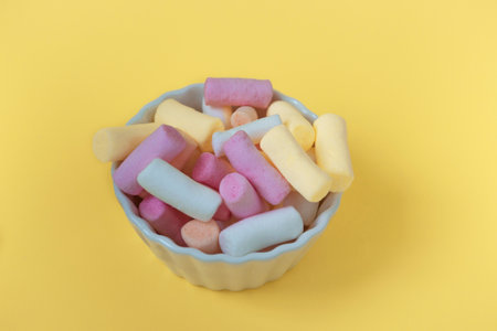 Multicolored marshmallows in a bowl on a yellow background. Mockup of packaging, postcard or card, close-up top viewの写真素材