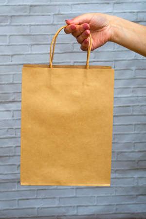 Mock up eco packaging close-up on a brick gray background. Kraft bag in a woman's hand. Online...