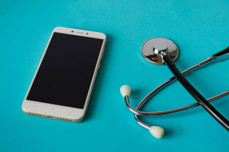 Medical concept: stethoscope and mobile phone on a bright blue background. House call. Ambulance. With copy space.の写真素材