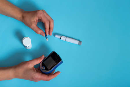 woman measures blood sugar with a glucometer.Diabetes concept on blue backgroundの写真素材