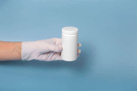Doctor's hand in medical gloves holds a tube of medicine or vitamins on a blue background. bottle mockupの写真素材