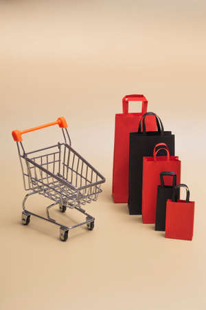 Black friday concept, mockup of paper black and red shopping bags with trolley on colored background. Black Friday sale. Vertical photoの写真素材